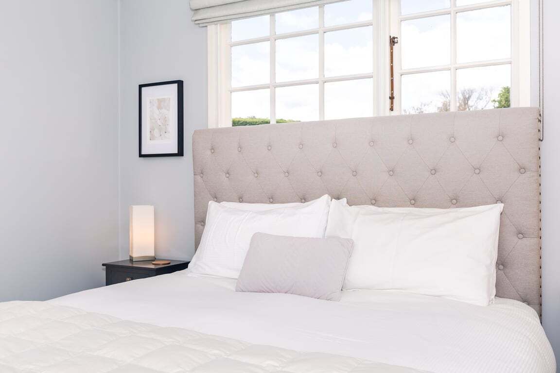 A bedroom with a large bed, a nightstand with a lamp, and a window with a view of greenery.