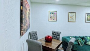 A dining area with a wooden table and four grey upholstered chairs, a red apple on the table, and a green sofa in the background. - Miami Oasis (Miami)