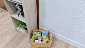 A corner of a room with a television, a wooden shelf unit, and a basket with books. - Miami Oasis (Miami)