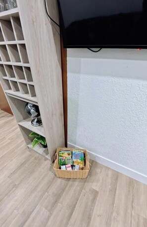 Ein Blick in einen Raum mit Fernseher, einer Holzregaleinrichtung und einem Korb voller Bücher.