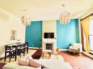 Ein Wohnzimmer mit türkisfarbenen Wänden, einem Kamin, einem Fernseher, einem Essbereich und einem Sofa.