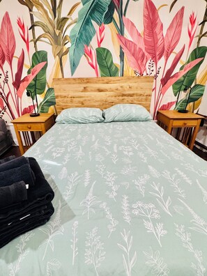 Ein Bett mit einem grünen, floralen Überwurf, einem Holz-Kopfstück und zwei Nachttischen mit Lampen.