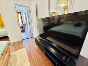 Ein Schlafzimmer mit einem großen Flachbildfernseher, Holzboden, einem Bett mit grüner Bettwäsche und einem gelben Teppich.