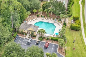 An aerial view of a property with a swimming pool surrounded by lounge chairs, a parking lot, and a building with a sloped roof. - Coastal Fairway Retreat, Sleeps 8, Pool! TPC Myrtle Beach across the street (Murrells Inlet)