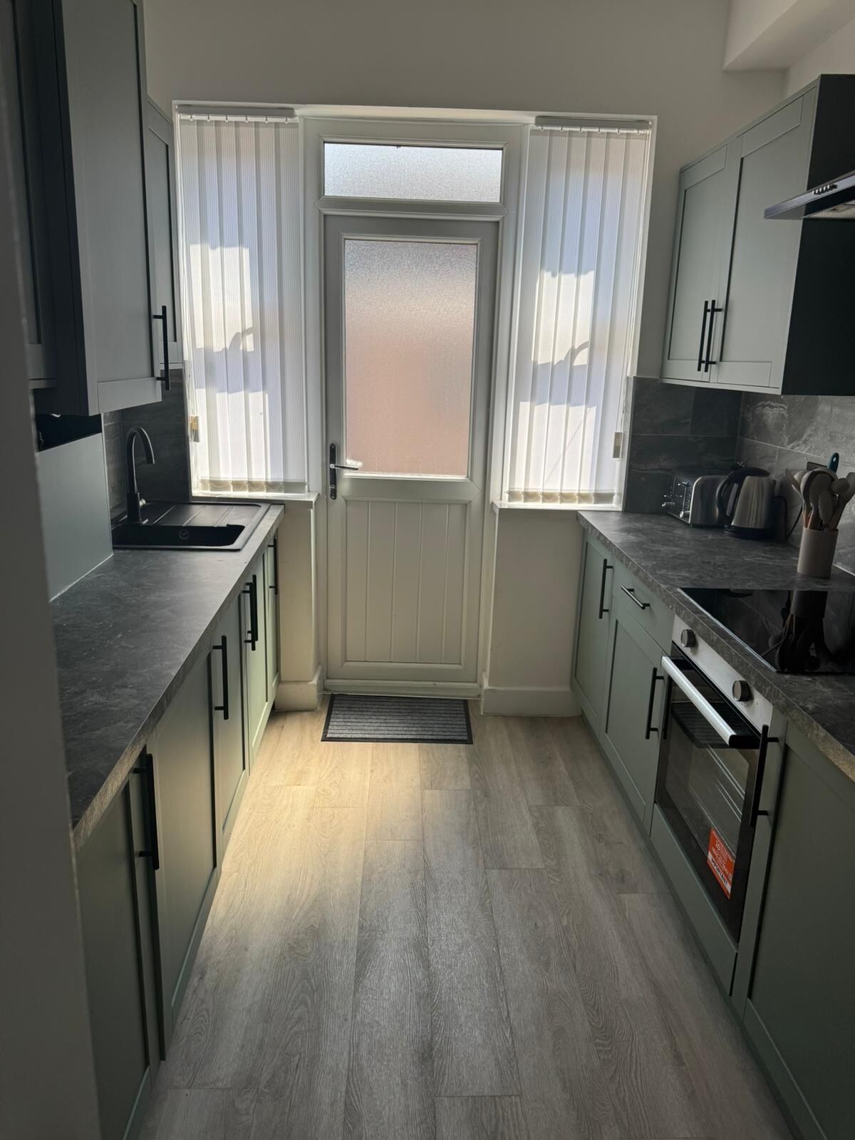 Una cocina compacta con una isla central, horno integrado y ventana con persianas.