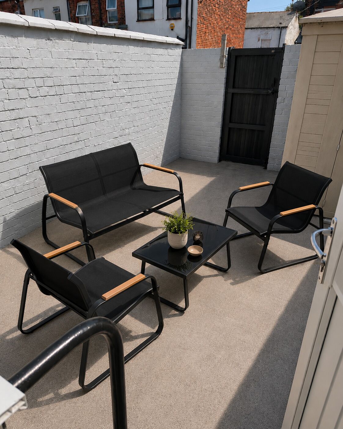 A patio with a black metal table, two black sofas with wooden armrests, and a potted plant.