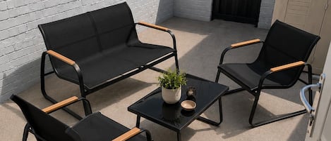 A patio with a black metal table, two black sofas with wooden armrests, and a potted plant.