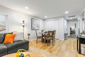 A modern living room with a grey sofa, a dining table with chairs, and a staircase leading to another level.