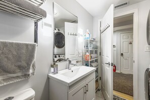 Ein kleines Badezimmer mit Waschbecken, Spiegel, Waschmaschine und Handtuchhalter.