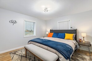 Une chambre à coucher comprenant un lit, des tables de chevet, un banc et un luminaire au plafond.