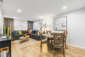 Ein modernes Wohnzimmer mit einer Eckcouch, einem Esstisch mit Stühlen und einem großen abstrakten Gemälde an der Wand.