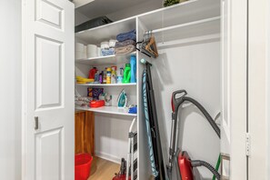 Un placard avec des étagères contenant des produits de nettoyage, un aspirateur et un seau rouge.