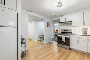 A modern kitchen with white cabinets, a stainless steel refrigerator, a built-in oven, and a dot-patterned backsplash.