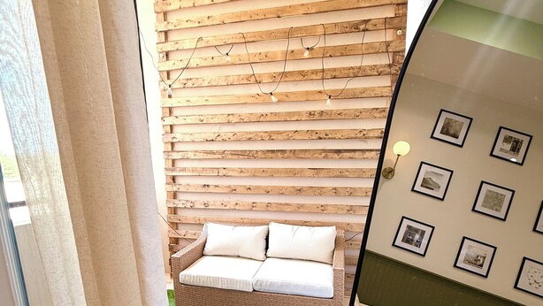 A room with a wooden slat wall, a sofa, a green artificial grass area, and a wall with framed pictures.