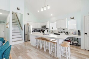 Une cuisine moderne dotée d’un îlot central, de tabourets de bar, d’un réfrigérateur en acier inoxydable et d’un escalier menant à un autre niveau.