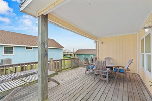 A covered deck with outdoor furniture, a wooden railing, and a view of neighboring houses. - Bolivar 5BR Beach House - Fenced - Steps to Beach (Bolivar Peninsula)