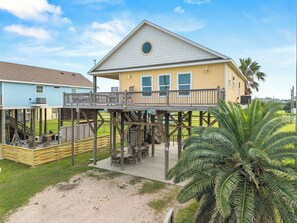 A two-story building with a balcony, outdoor seating, and a palm tree. - Bolivar 5BR Beach House - Fenced - Steps to Beach (Bolivar Peninsula)