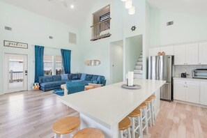 A modern kitchen with white cabinets, a stainless steel refrigerator, and a bar area with stools. - Bolivar 5BR Beach House - Fenced - Steps to Beach (Bolivar Peninsula)