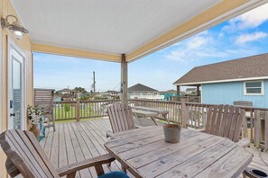 Eine Holzterrasse mit Tisch und Stühlen, ein überdachter Bereich mit Geländer und Blick auf benachbarte Häuser.