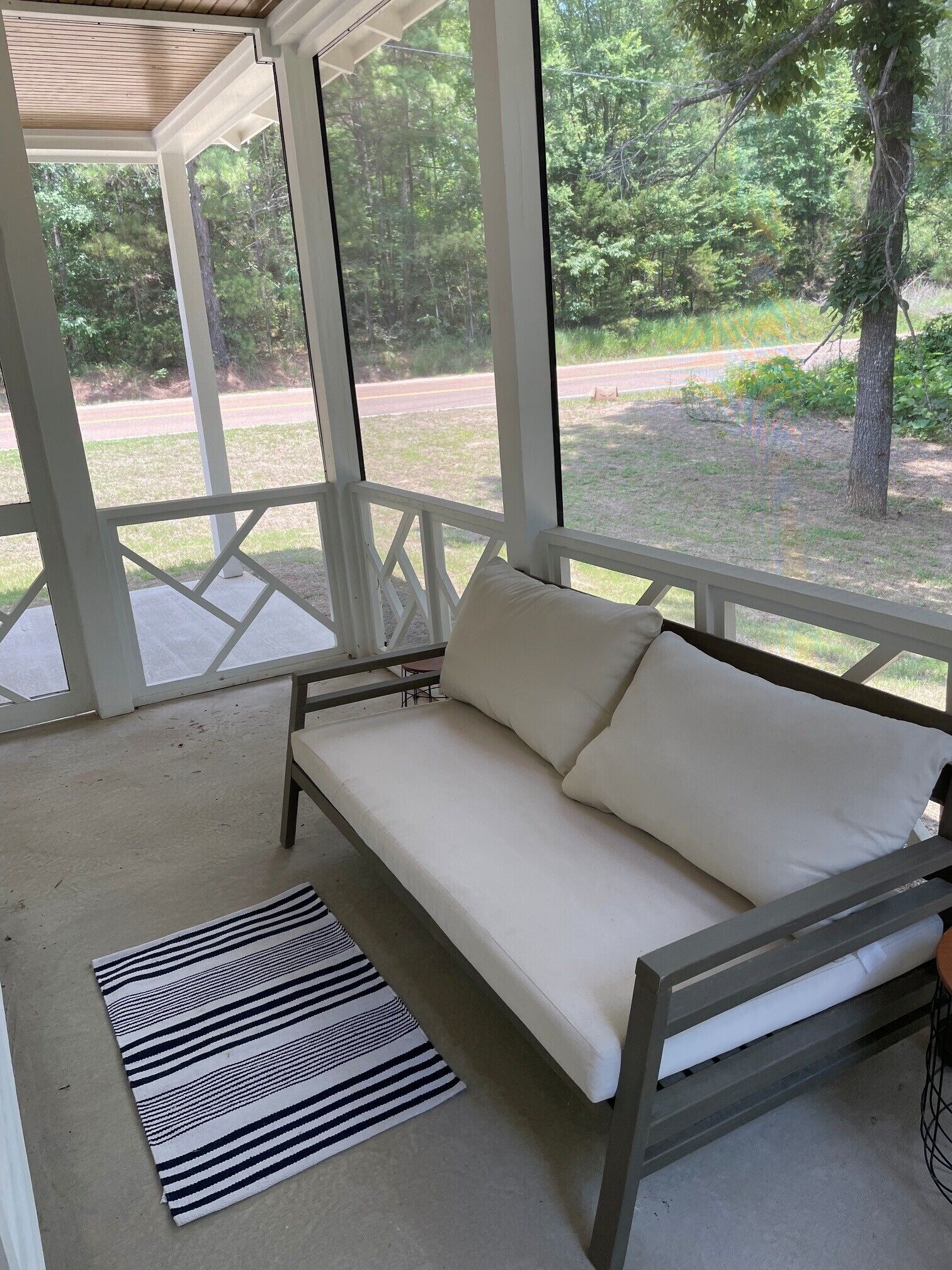 A covered outdoor seating area with a sofa and a striped rug.