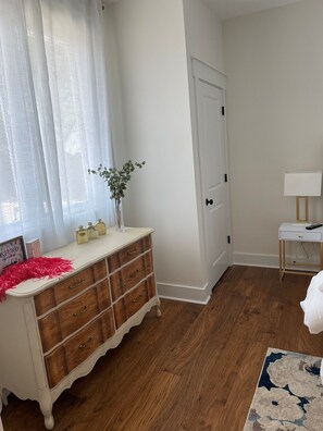 Ein Zimmer mit einem Holzkoffer, einer weißen Tür, einem kleinen Nachttisch mit Lampe und einem gemusterten Teppich.