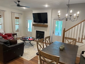 A living room with a fireplace, a television mounted above it, a dining table with chairs, a red leather sofa, and a ceiling fan. - 3-Bdrm Oxford Home Away From Home 6 mins to The Square, 3.9 miles to The Stadium (Oxford)