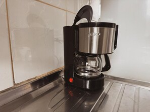 Eine schwarze Kaffeemaschine mit transparentem Wasserbehälter und einem Edelstahlkessel auf einer Küchenarbeitsplatte.