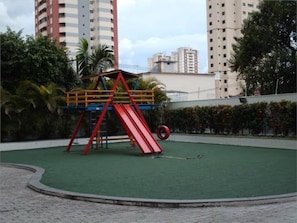 A playground with a red slide and a climbing structure, surrounded by a paved area and greenery. - Apartment in Tatuapé, Bragança mountain range, x Itapura (São Paulo)