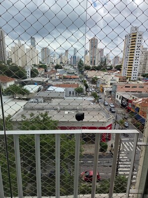 A cityscape viewed through a chain-link fence with buildings, roads, and a crosswalk. - Apartment in Tatuapé, Bragança mountain range, x Itapura (São Paulo)