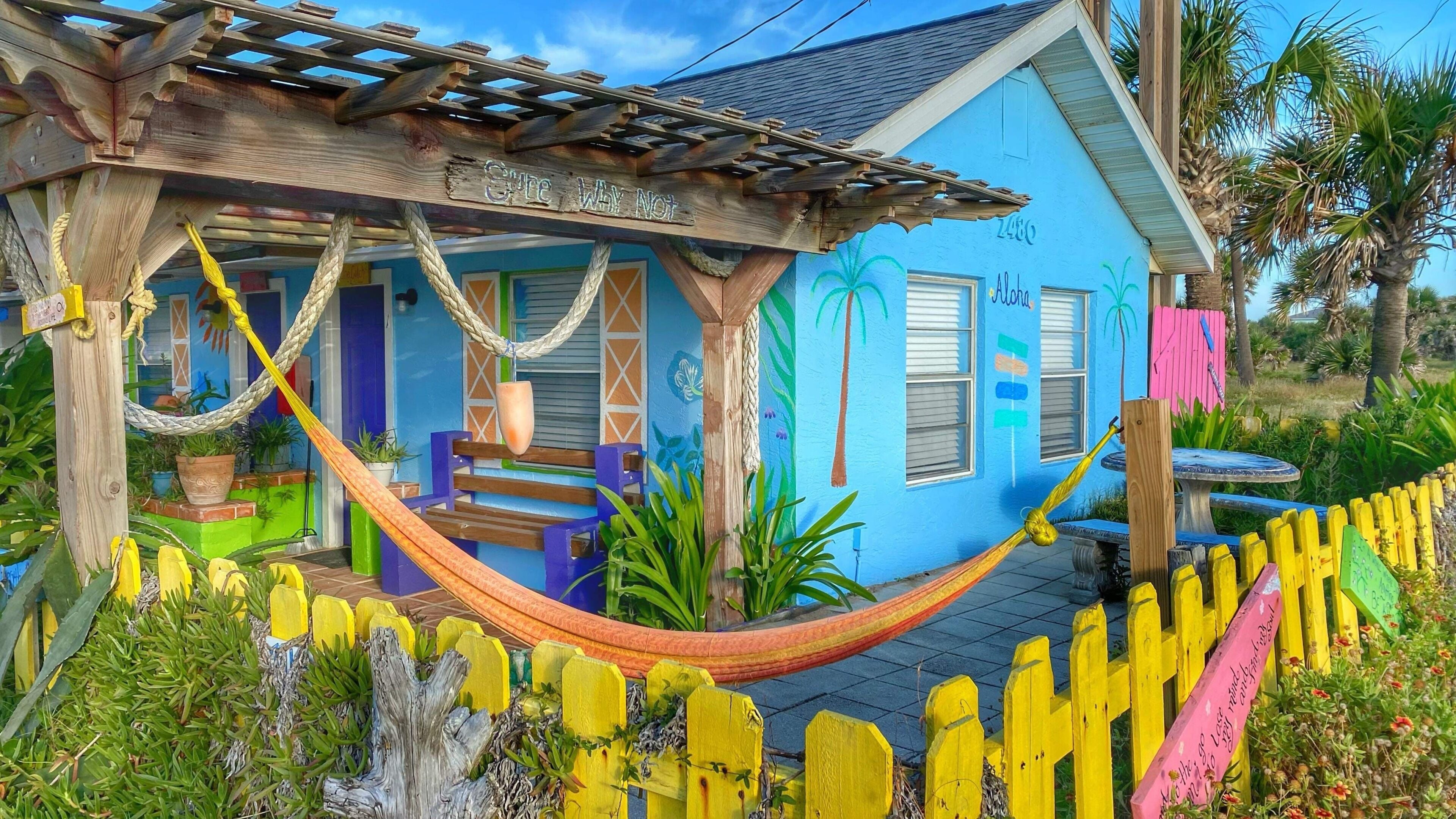 Una casa colorida con una hamaca, una valla de madera y un jardín.