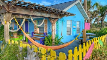 Una casa colorida con una hamaca, una valla de madera y un jardín.