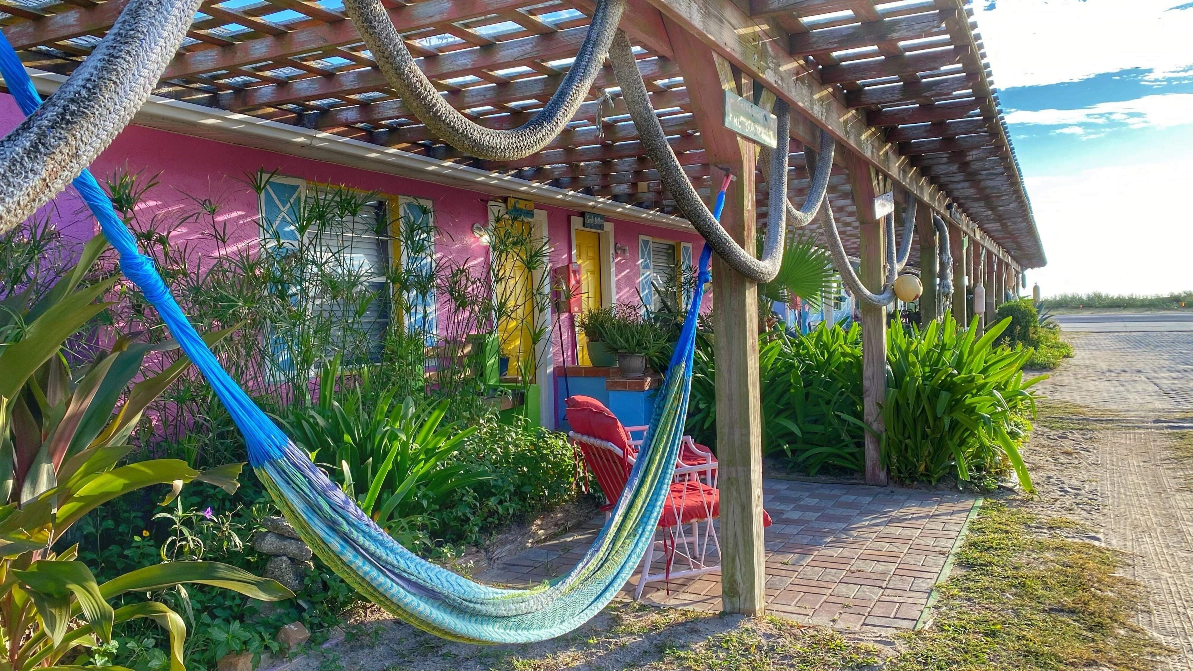 A colorful building with a hammock, potted plants, and a paved walkway.