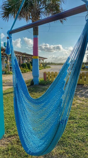 A hammock hanging between two poles with a palm tree and a building in the background. - Si Como No Inm (Flagler Beach)