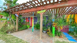 A covered patio area with a wooden pergola, potted plants, and a brick pathway.