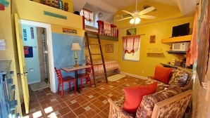 A compact room with a bunk bed, a small table with chairs, a ceiling fan, and a microwave on a shelf.