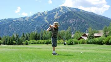 A child playing golf on a green field with a mountain in the background.