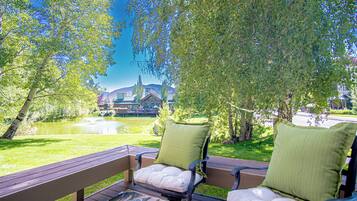 An outdoor seating area with two chairs and a table, overlooking a pond and a building with a tower.