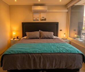 A hotel room with a bed, nightstands, a window with a view, and an air conditioning unit. - Edificio Eleuterio by Domus Travels (Santiago)