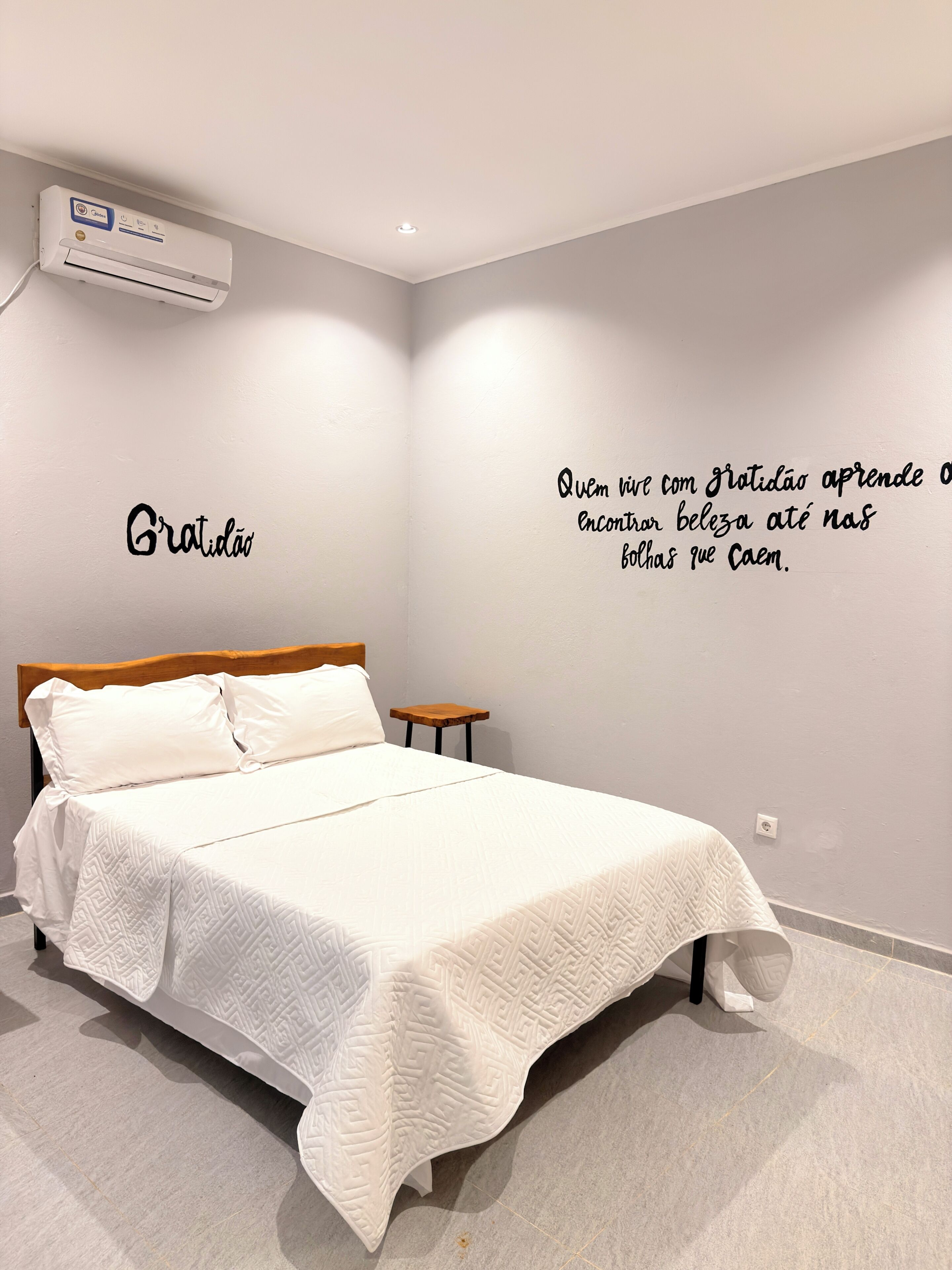 Une chambre à coucher comprenant un lit, une table de chevet, un climatiseur fixé au mur et une citation inspirante sur le mur.