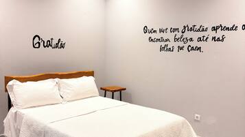Une chambre à coucher comprenant un lit, une table de chevet, un climatiseur fixé au mur et une citation inspirante sur le mur.