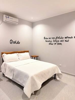 A bedroom with a bed, a nightstand, a wall-mounted air conditioner, and a motivational quote on the wall.