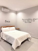 A bedroom with a bed, a nightstand, a wall-mounted air conditioner, and a motivational quote on the wall.