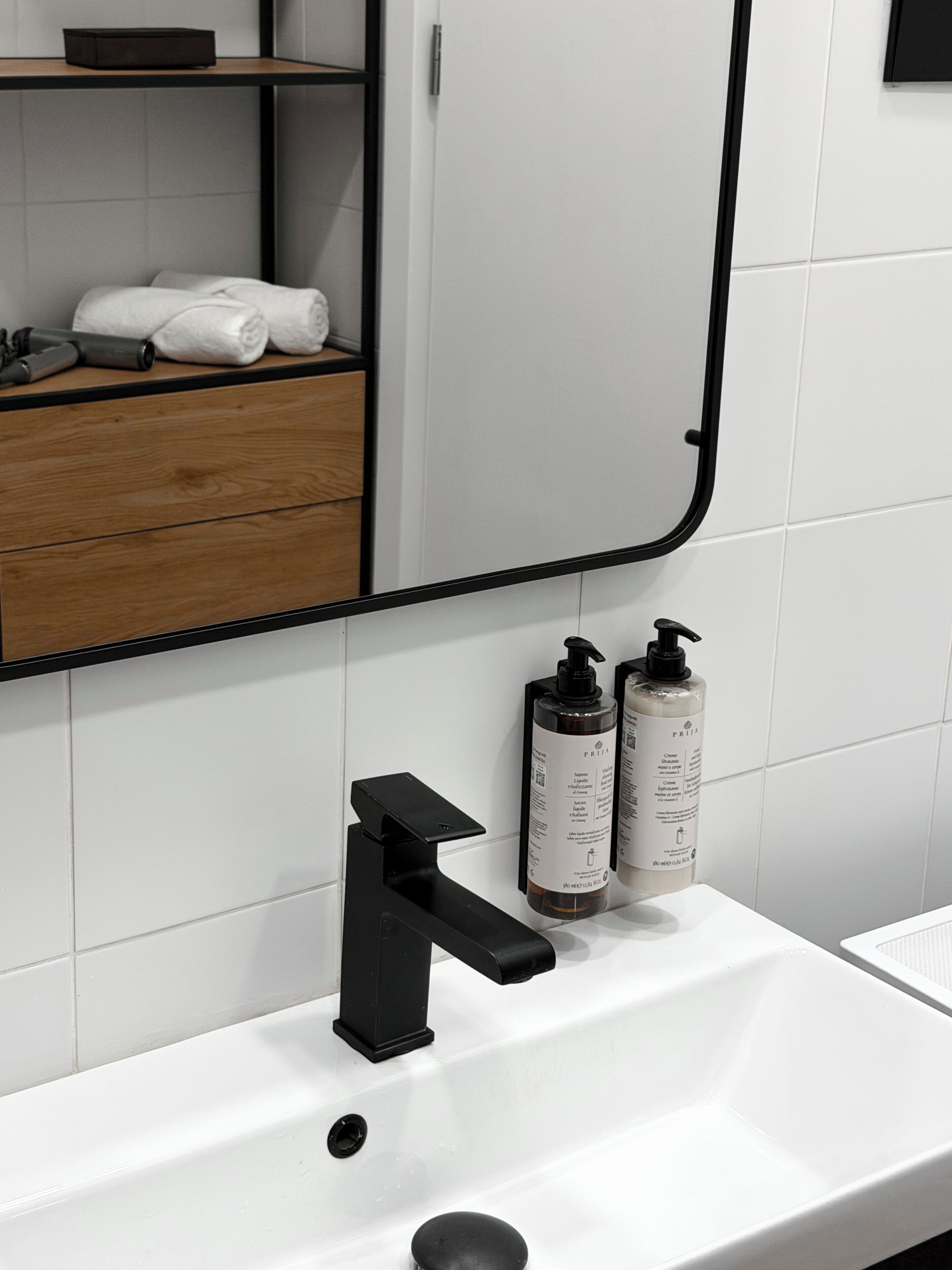 A modern bathroom with a white sink, black faucet, and two bottles of shampoo.