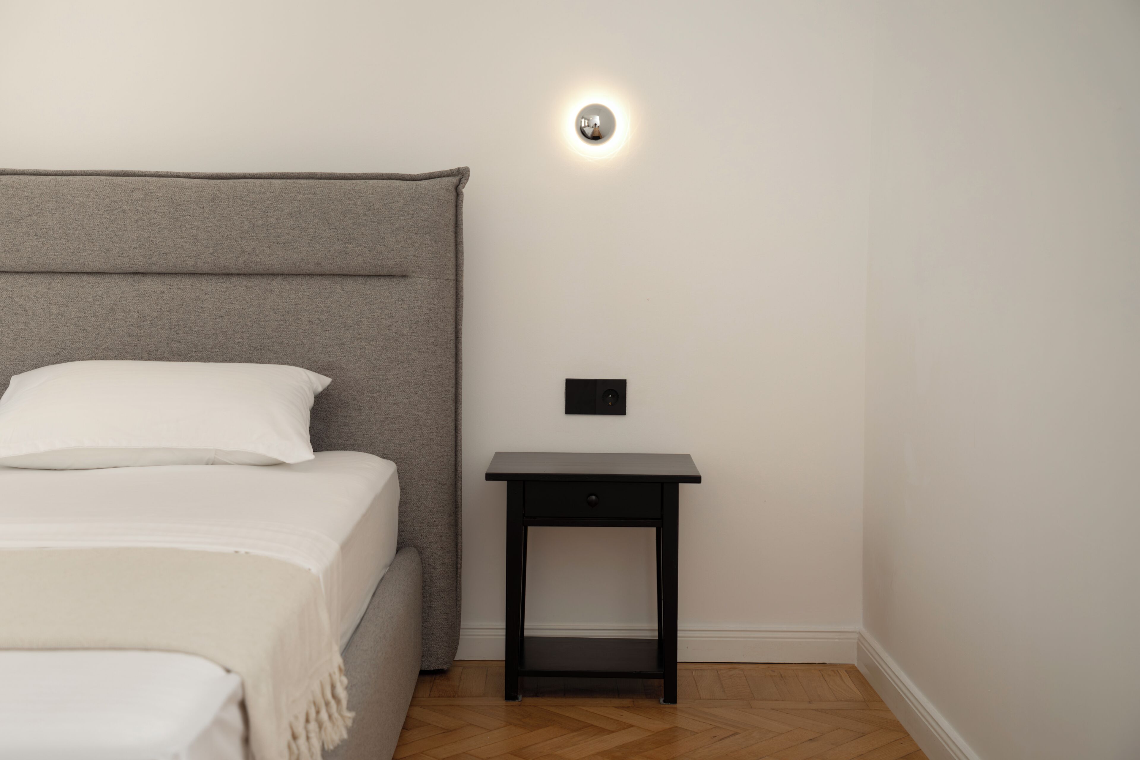 A bedroom with a bed, a bedside table, and a wall-mounted light fixture.