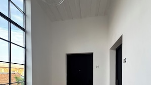Una habitación con un ventanal grande, suelo de madera, una puerta negra y el número '01' en la pared.