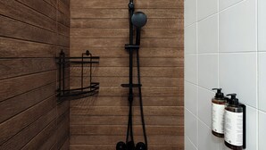 Ducha con pared de paneles de madera, un cabezal de ducha negro y dos botellas de champú en la pared.
