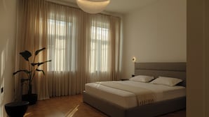 Un dormitorio con cama, cortinas, una planta en maceta y una mesita de noche.