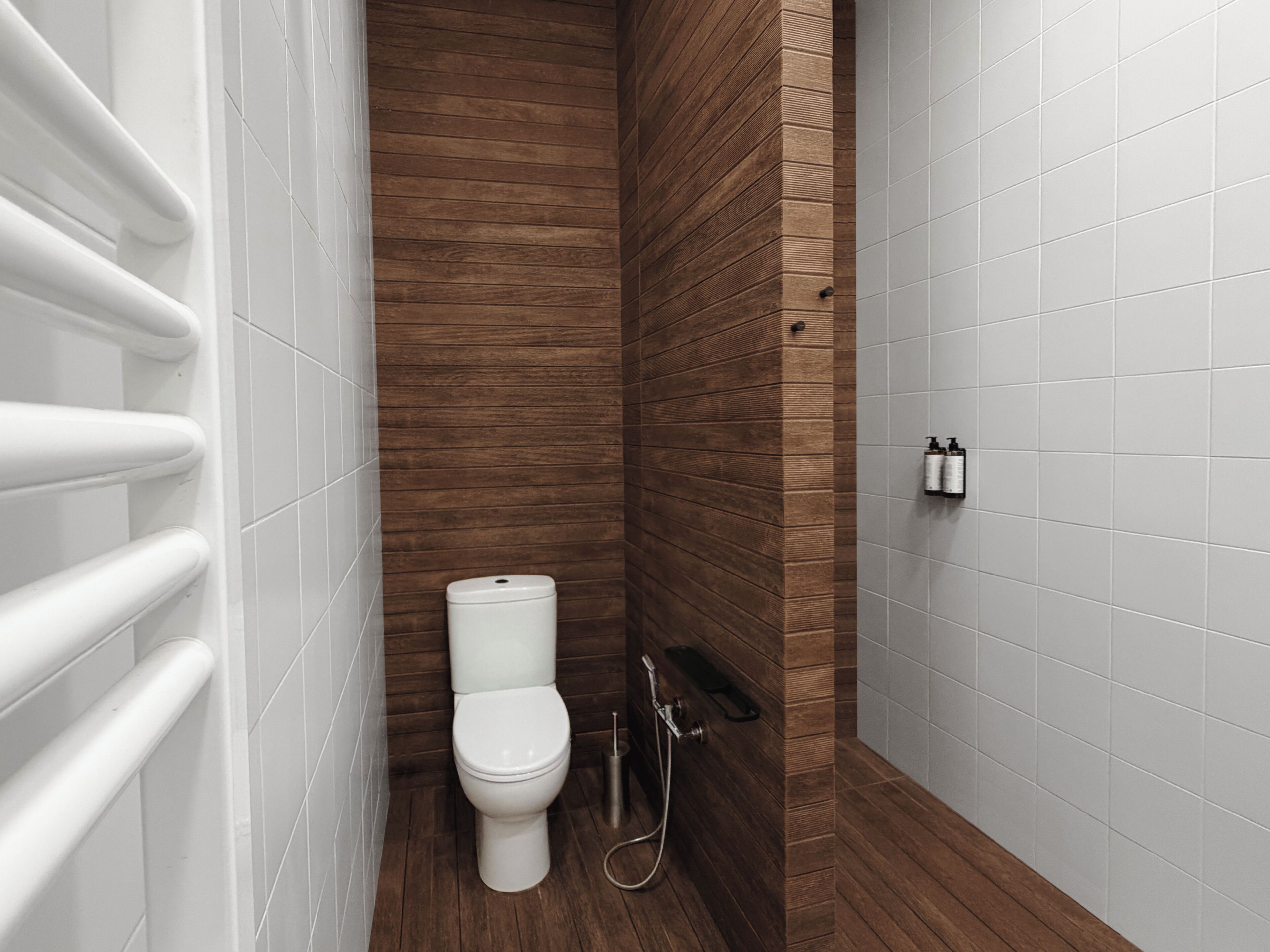 A bathroom with a wooden accent wall, a white toilet, a shower, and a hand dryer.