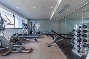 Ein Fitnessstudio mit Laufbändern, Crosstrainern, einem stationären Fahrrad und einer Hantelbank.
