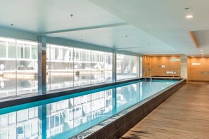 A long indoor swimming pool with clear glass walls, wooden flooring, and a modern design. - Smart Compact Two Bedrooms 2 Bath & Two Balconies (Auckland City)
